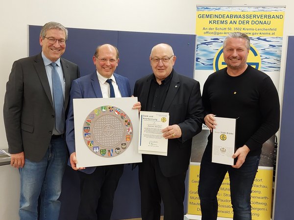 Vier Männer stehen vor einem Banner des Gemeindeabwasserverbands Krems an der Donau und halten Auszeichnungen sowie eine Plakette mit Wappen.