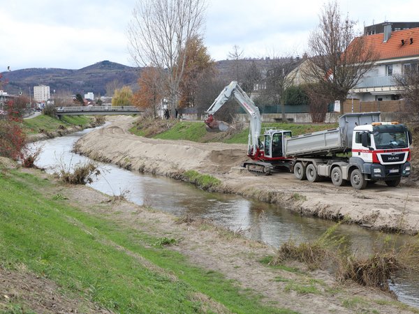 Ein Bagger schaufelt neben dem Kremsfluss Schotter auf einen Lkw