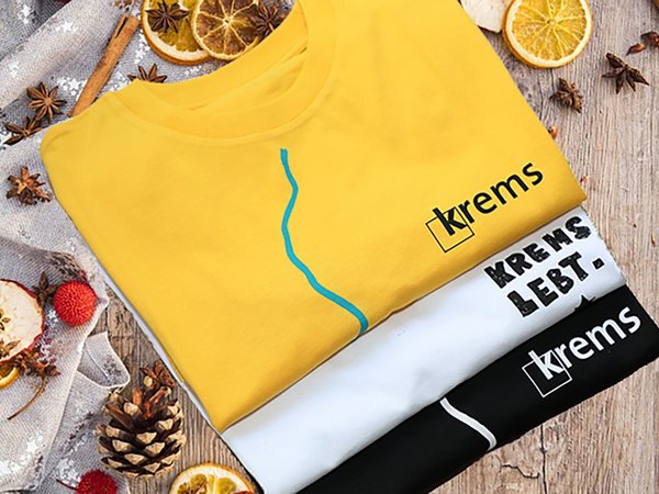 Drei Krems T-Shirts liegen gefaltet auf einem weihnachtlich dekorierten Tisch